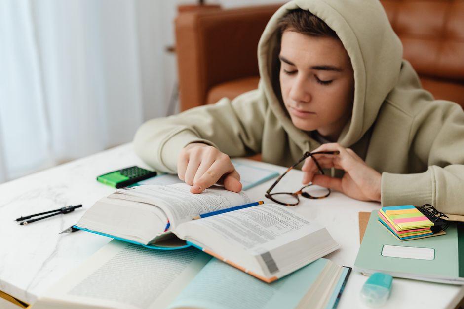 Adolescent qui révise ses maths dans un manuel ouvert sur son bureau